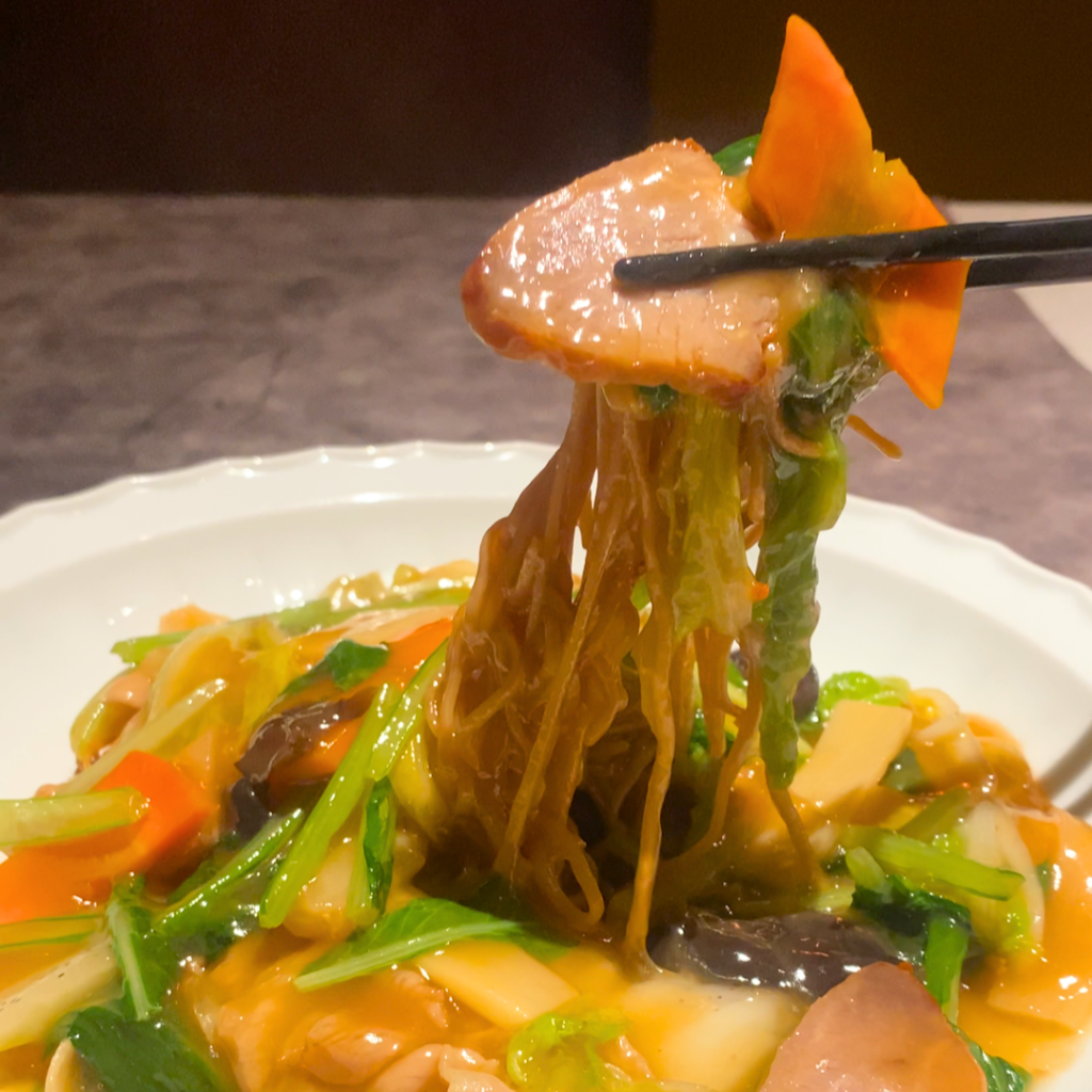 肉餡が絡む焼きそばを箸で持ち上げる様子。もちもち麺とコク深い餡が食欲をそそる。
