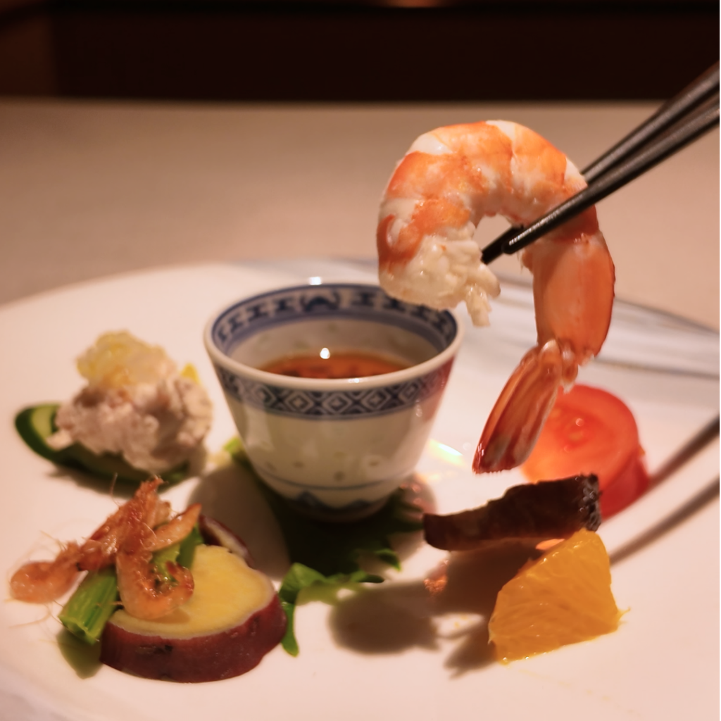 春の彩りを添えた立春の前菜盛り合わせ。お箸で海老を持ち上げた瞬間を切り取ったカットで、透明感のある海老と華やかな前菜が映える季節の中華前菜皿。