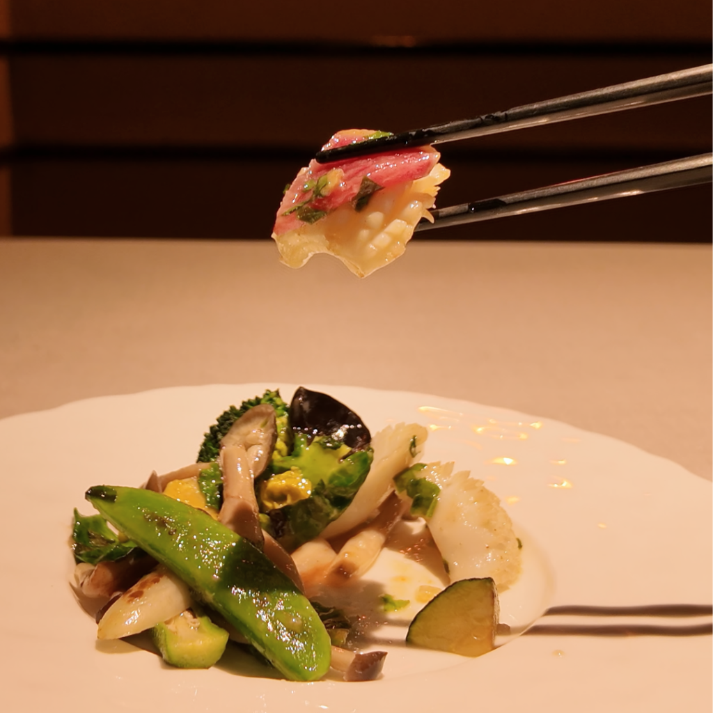 甲烏賊と春野菜の紫蘇炒めから、箸で烏賊と彩り豊かな野菜を持ち上げた瞬間を捉えた写真。紫蘇の香りと春らしい軽やかさが伝わる、季節の中華料理の臨場感あるカット。