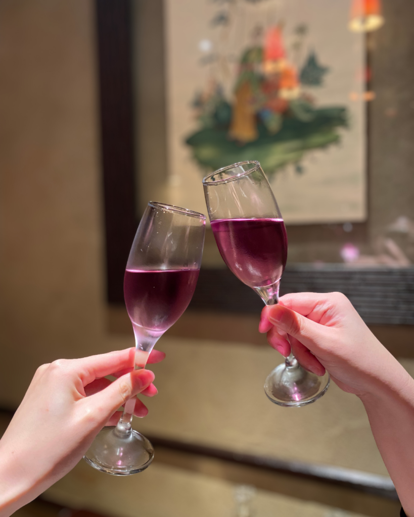 当店おすすめの紫ワインで乾杯するシーン。グラス越しに華やかな色彩が広がる