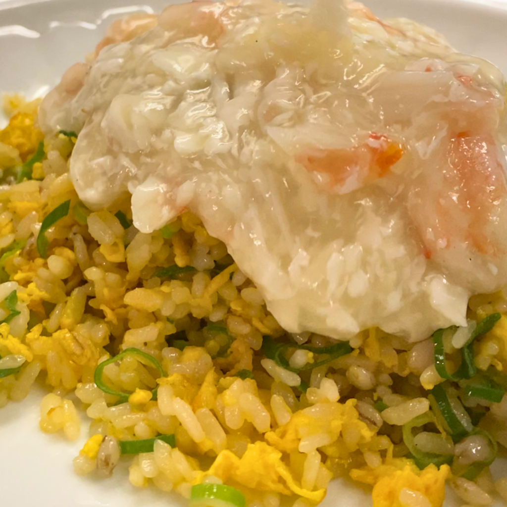 蟹肉たっぷり餡かけ炒飯に熱い蟹餡をかけ、餡が広がっていく様子を写した写真。とろみ餡と炒飯の質感が分かる2月限定メニューの調理の仕上げのシーン。