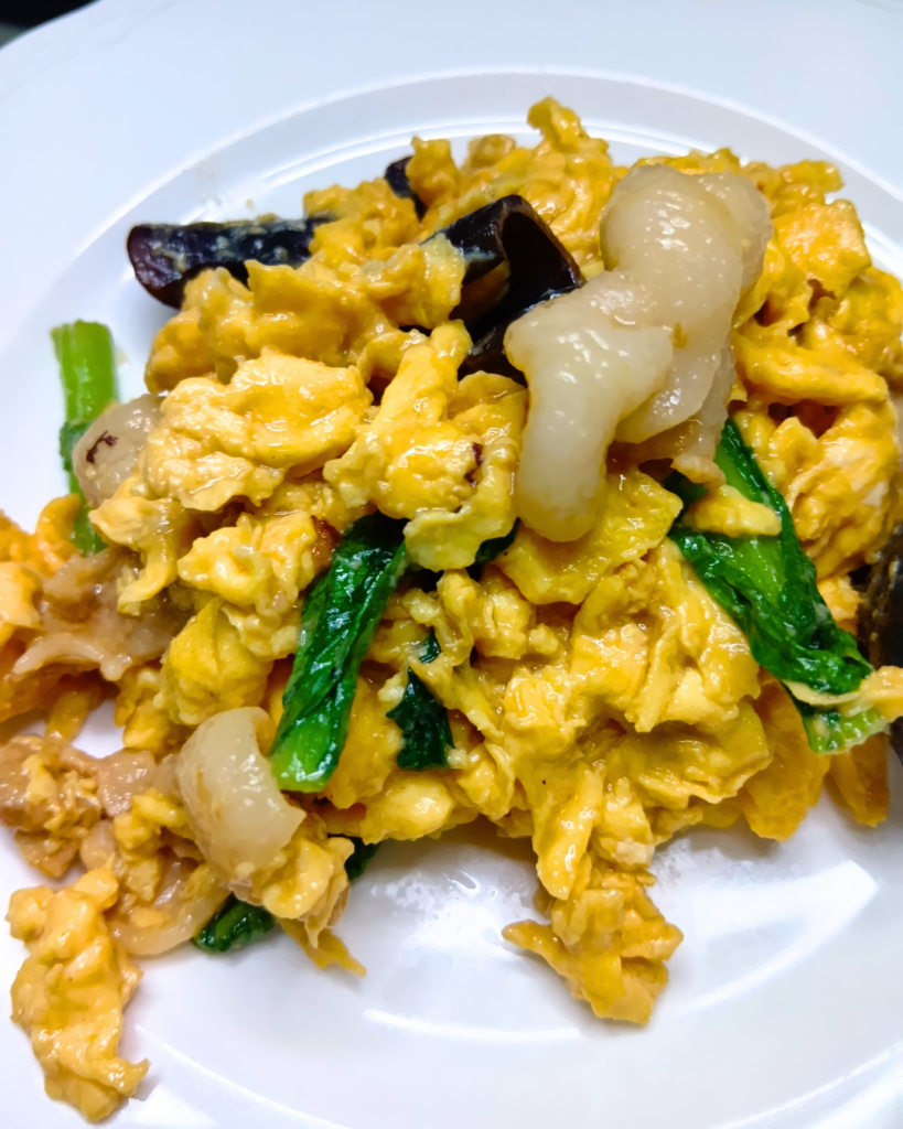 ふんわりとした黄色い玉子に豚バラのツヤが映え、黒いきくらげと緑の葉ものが彩る木須肉のアップ写真。具材のコントラストが鮮やかで、ふっくらした質感が伝わる一皿。