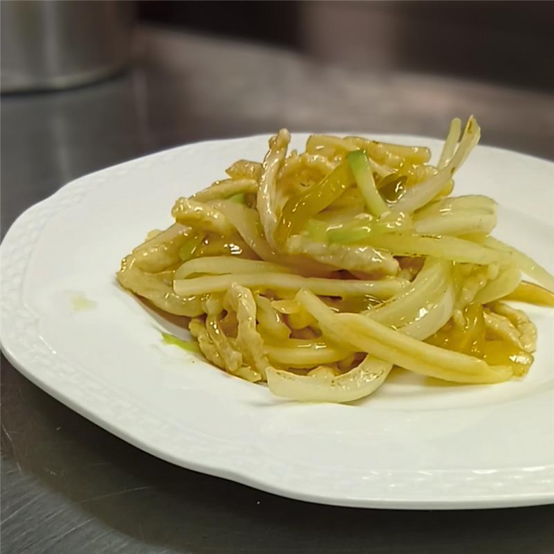 調理台の上に置かれた白皿いっぱいに、ツヤのある細切りの豚肉と搾菜が盛られた炒め物。素材の光沢とボリューム感が際立つ写真。