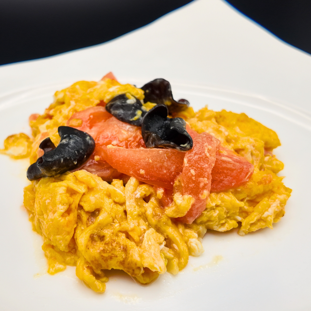 完熟トマトとふんわり玉子を炒め合わせた『トマトと玉子の炒め』のアップ写真。鮮やかな赤と黄色の対比が美しく、優しい家庭料理の温かさが伝わる一皿。