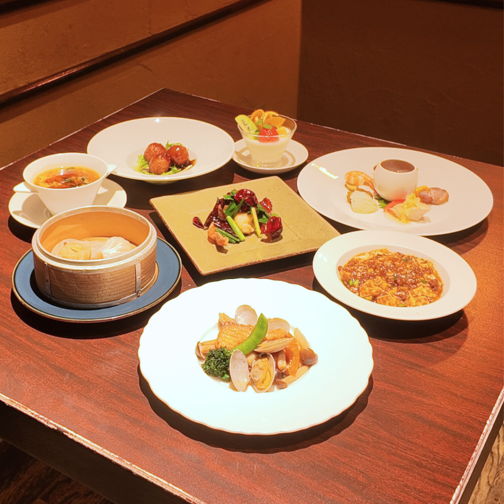  春風（はるかぜ）コースの全景。前菜、点心、海鮮、肉料理、麺・飯、デザートが大皿で並ぶ、春の歓送迎会向けシェアスタイル。