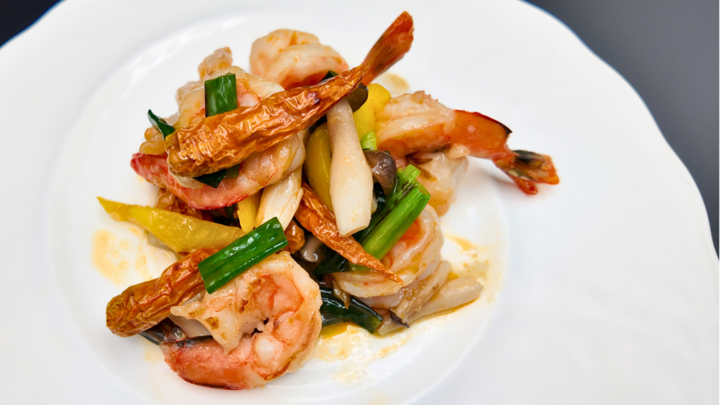 大海老と黄色唐辛子の炒め物を真上から撮影した料理写真。大きな海老と鮮やかな黄色唐辛子が皿全体に美しく盛り付けられている。